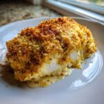 Close up of a baked caesar chicken breast with a thick, golden, crispy breadcrumb crust and creamy sauce oozing out.
