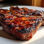 Close-up of two perfectly grilled, glazed pork steak cuts with visible char marks on a white plate.