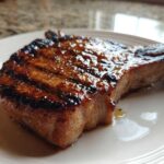 Close-up of a thick, grilled pork chop showing char marks and a glossy marinade for pork chops.