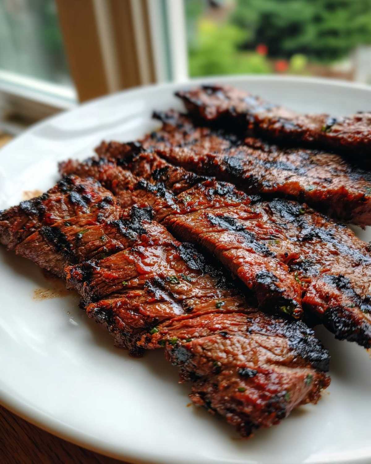 Close-up of perfectly grilled and sliced steak coated in a rich carne asada marinade, resting on a white plate.