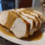 Close-up of sliced, juicy instant pot turkey breast drizzled with savory brown gravy on a white plate.