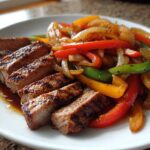 Close-up of perfectly grilled and sliced steak fajitas served with colorful sautéed bell peppers and onions on a white plate.