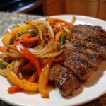 Close-up of sliced, grilled steak served next to colorful sautéed onions and bell peppers for steak fajitas.