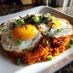A vibrant plate of kimchi fried rice topped with two sunny-side-up eggs, seaweed, and green onions.