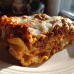 A close-up, sunlit slice of Lasagna with Cottage Cheese showing layers of pasta, meat sauce, and melted cheese topping.