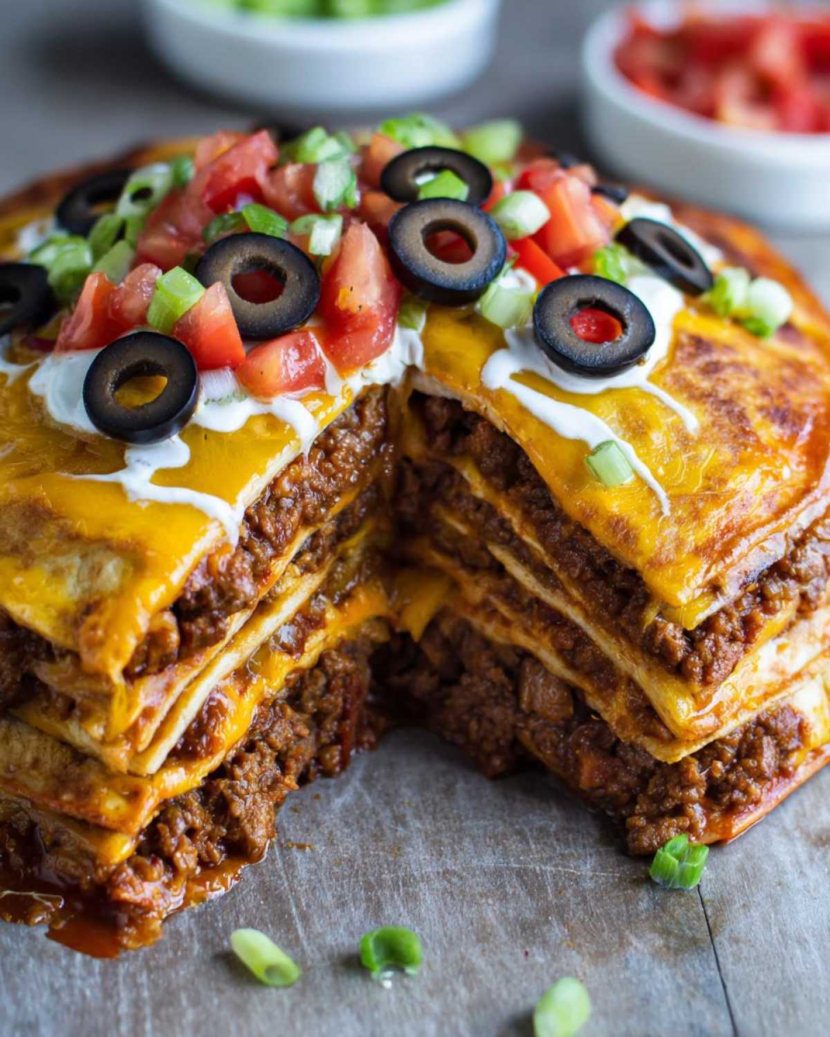 A cross-section view of a tall, layered mexican pizza filled with seasoned ground beef and melted cheese, topped with sour cream, tomatoes, olives, and green onions.