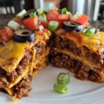 A thick slice of layered Mexican pizza showing layers of seasoned ground beef, tortillas, melted cheese, and fresh toppings like olives and tomatoes.