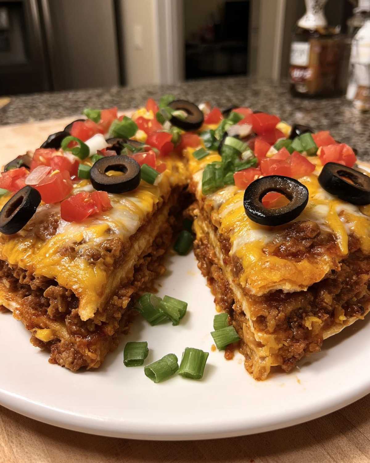 A slice cut from a layered Mexican pizza showing seasoned ground beef, melted cheese, and fresh toppings like olives and tomatoes.