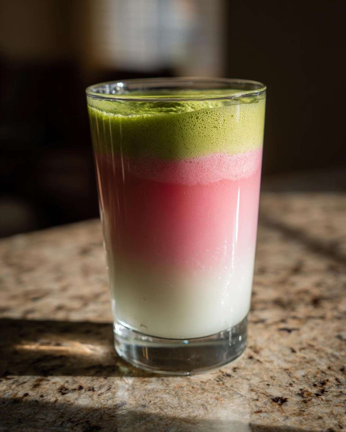 A layered strawberry matcha latte showing distinct green, pink, and white layers in a tall glass.