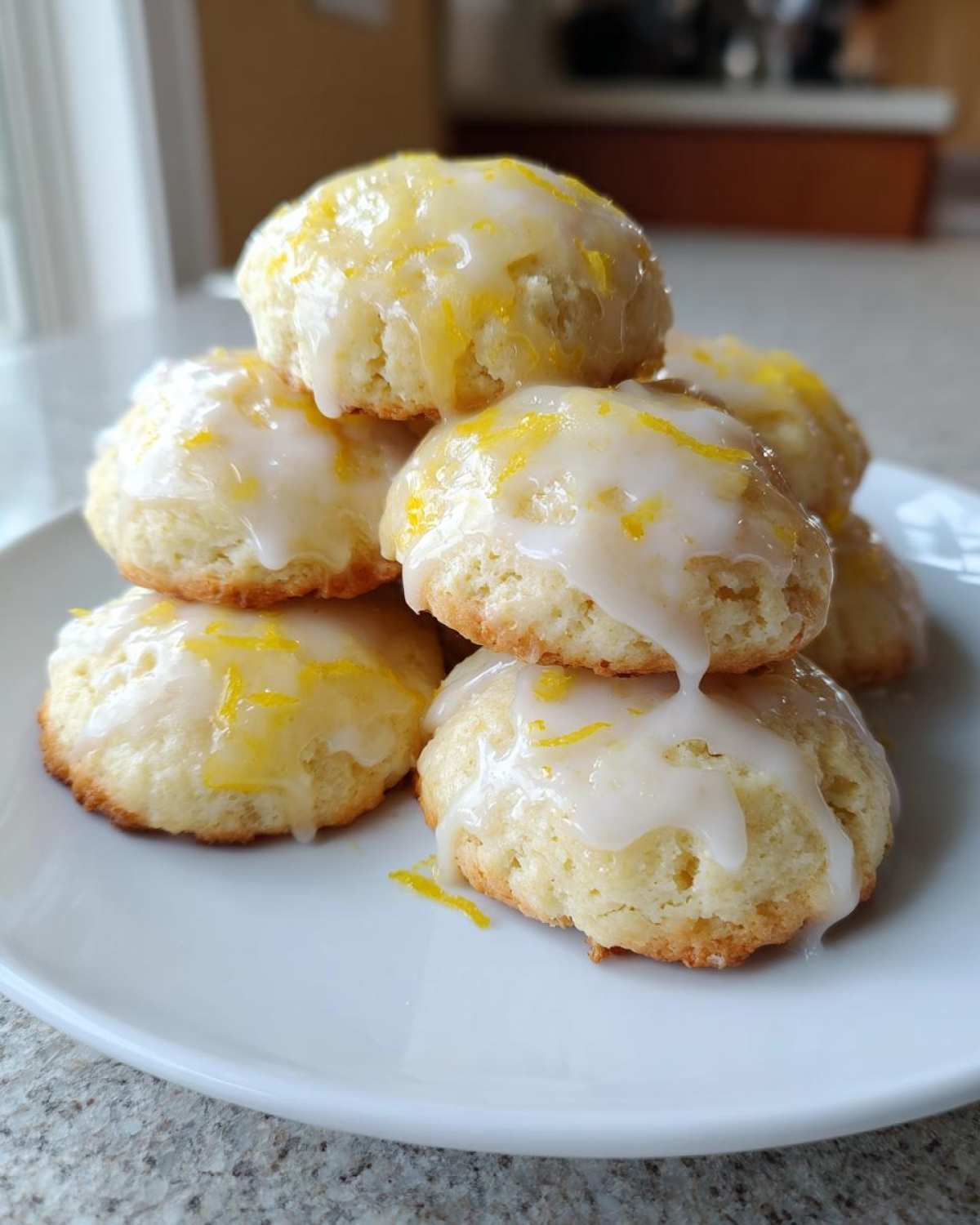 A stack of soft, glazed italian ricotta cookies topped with bright yellow lemon zest.
