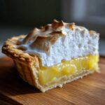 Close-up of a perfect slice of lemon meringue pie showing the flaky crust, bright yellow filling, and toasted meringue.