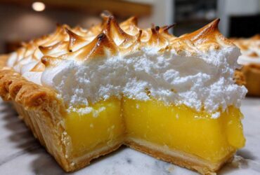 Close-up of a thick slice of lemon meringue pie showing bright yellow curd and tall, torched meringue peaks.