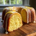 A slice cut from a bundt-style lemon pound cake, drizzled with a thick glaze and lemon zest.