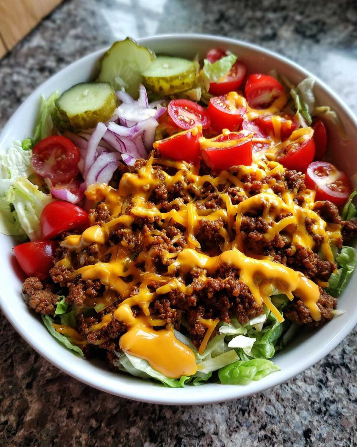 A close-up of a delicious cheeseburger bowl featuring seasoned ground beef, melted cheddar cheese, lettuce, tomatoes, pickles, and onions.