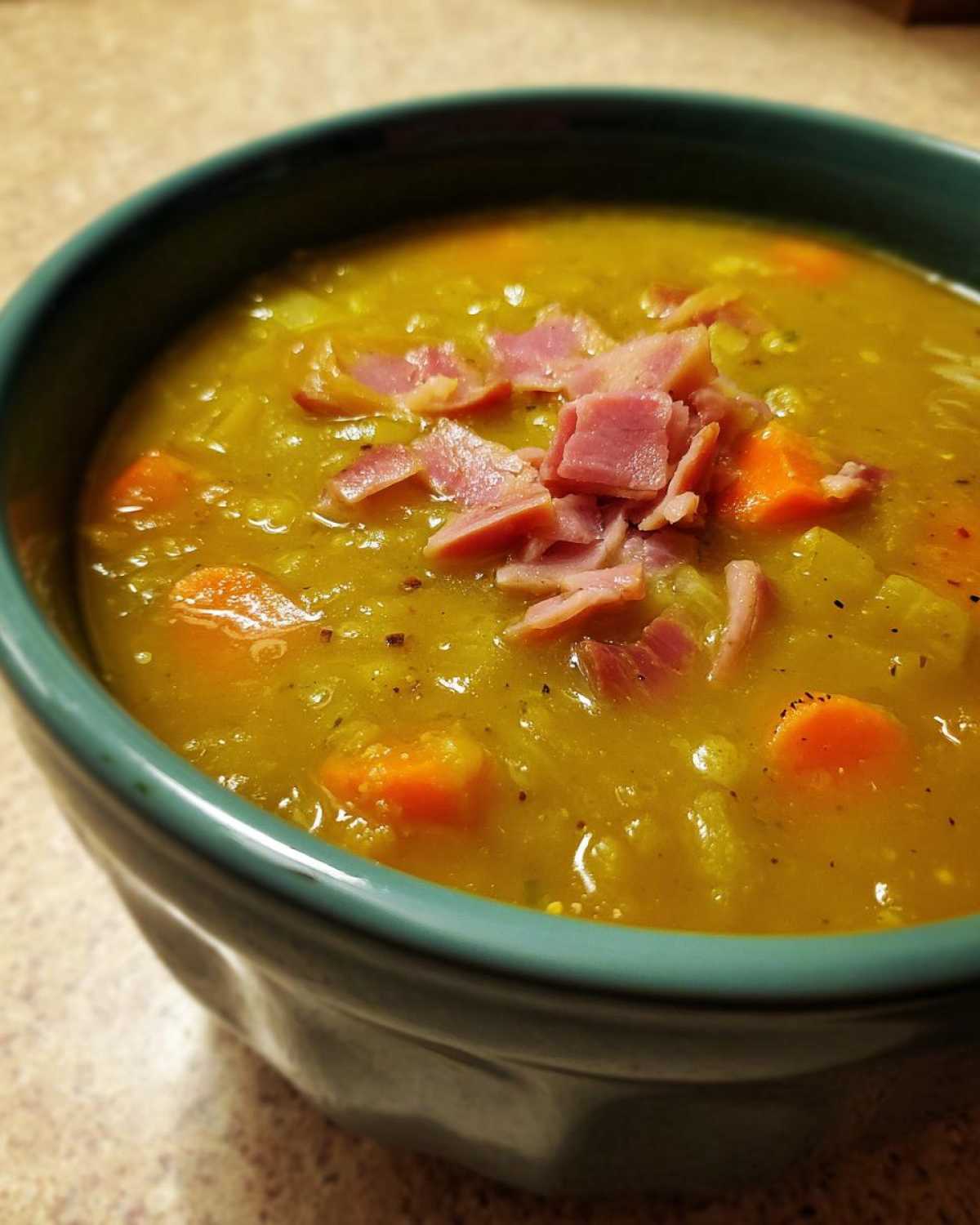 Close-up of a thick, yellow pea soup topped with diced ham and visible chunks of carrot.
