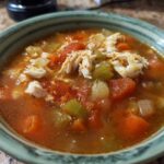 A close-up of a bowl of savory maryland crab soup, featuring chunks of crab meat, tomatoes, carrots, and celery in a rich broth.