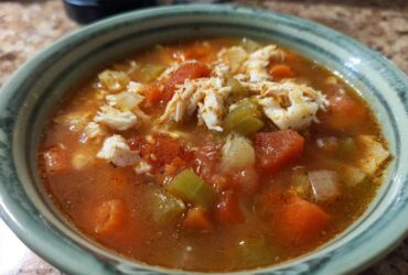 A close-up of a bowl of savory maryland crab soup, featuring chunks of crab meat, tomatoes, carrots, and celery in a rich broth.