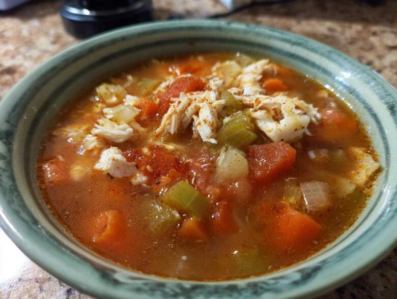 A close-up of a bowl of savory maryland crab soup, featuring chunks of crab meat, tomatoes, carrots, and celery in a rich broth.