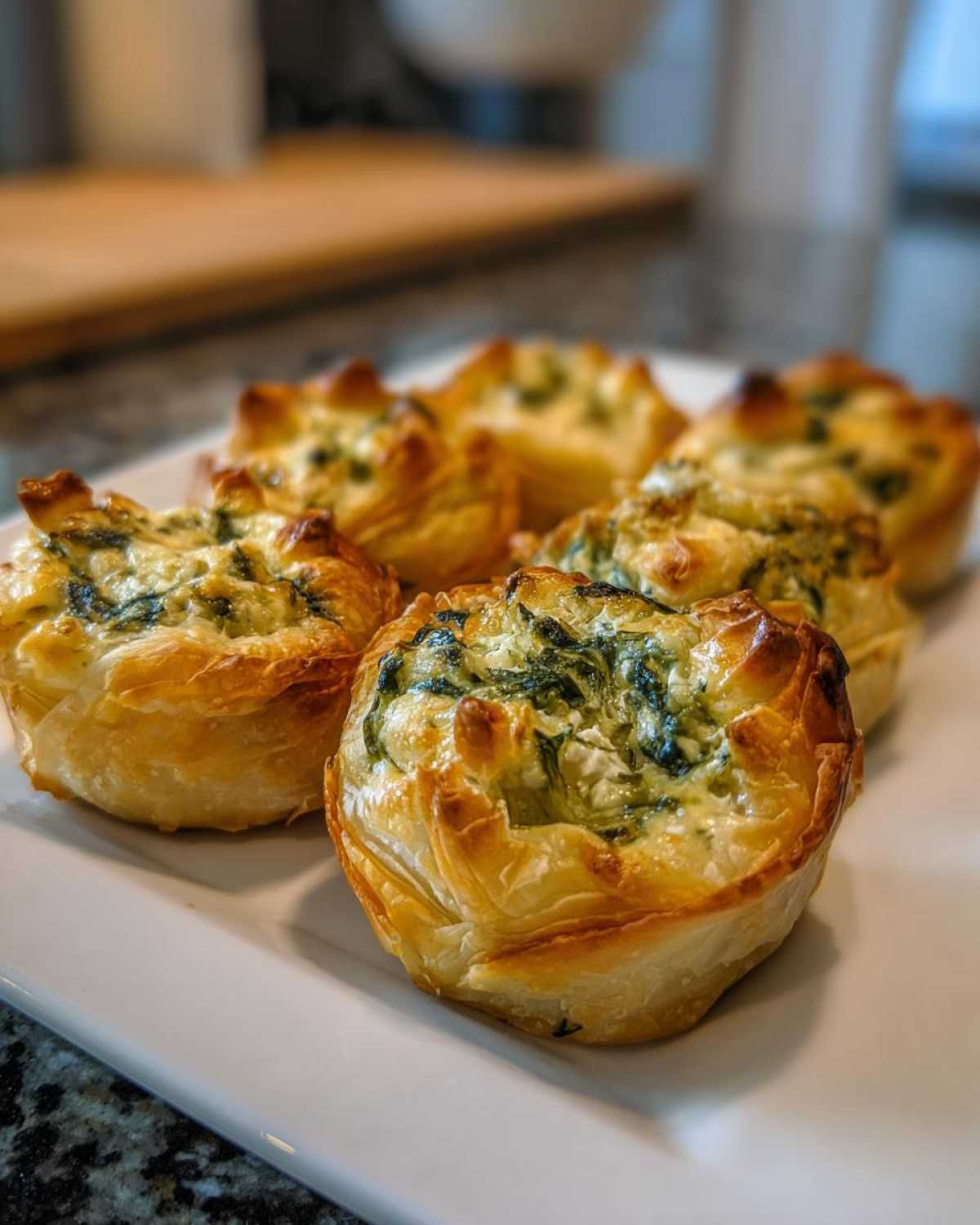 Close-up of golden baked Mediterranean Spinach and Feta Cheese Crisps served on a white rectangular plate.