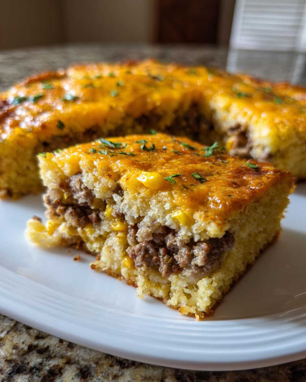 A square slice of Mexican cornbread casserole showing a savory ground meat filling, served on a white plate.