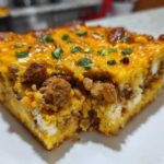 Close-up of a hearty slice of mexican cornbread casserole topped with melted cheddar cheese and green onions.