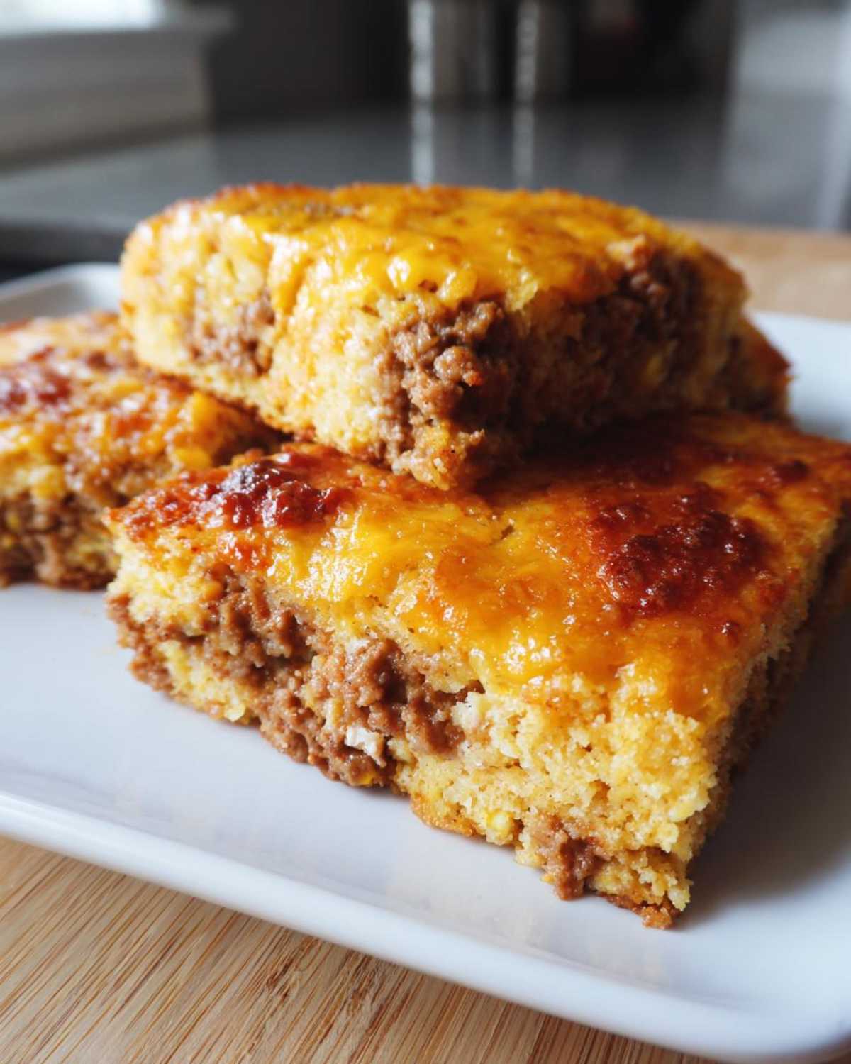 Three stacked squares of Mexican cornbread casserole featuring a layer of seasoned ground meat and a melted, bubbly cheddar cheese topping.