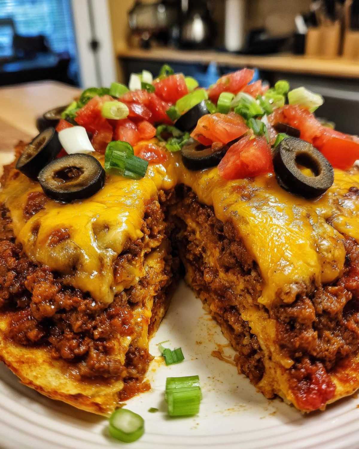 A cross-section view of a thick, layered Mexican pizza topped with melted cheese, tomatoes, olives, and green onions.