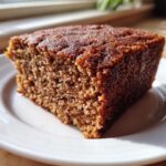 Close-up of a moist, dark brown slice of applesauce cake on a white plate.
