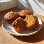Close-up of three golden brown bran muffins on a plate, one split open showing the moist interior texture.