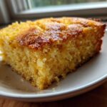 A close-up of a thick, moist slice of golden buttermilk cornbread resting on a small white plate.