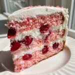 Close-up of a moist slice of 3-layer cherry cake showing pink sponge, white frosting, and whole cherries.