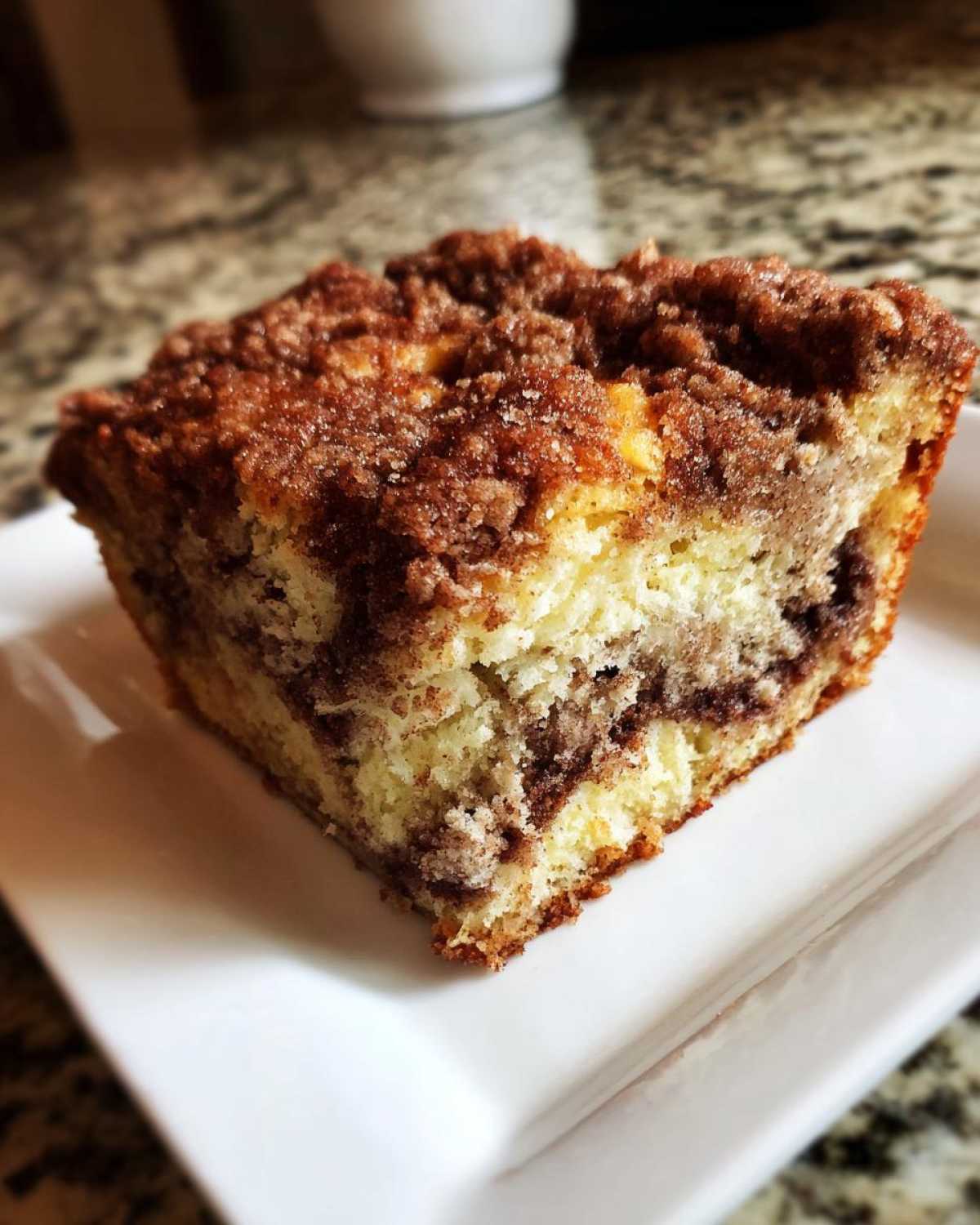 Close-up of a moist slice of coffee cake featuring a yellow crumb, cinnamon swirl, and thick streusel topping.