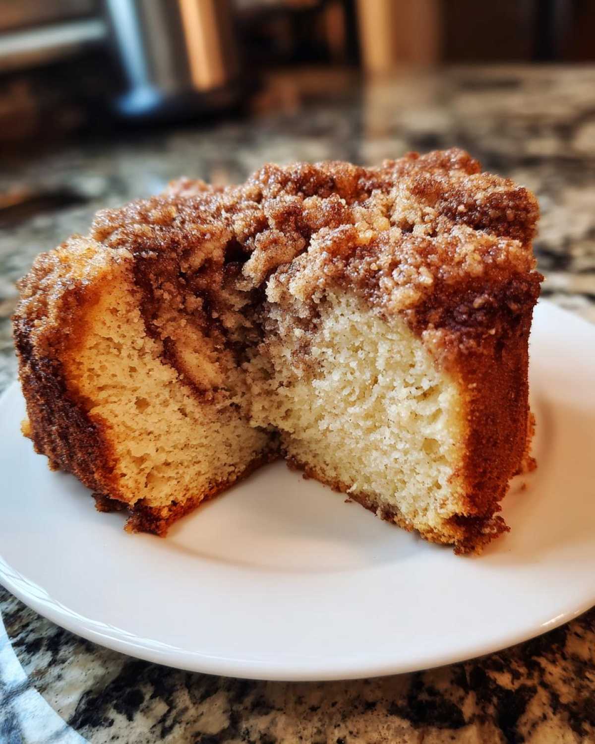 A thick slice of moist coffee cake, cut in half to show the crumb topping and tender interior.