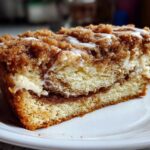Close-up of a moist slice of coffee cake featuring layers of cake, cream cheese filling, and a thick cinnamon streusel topping.
