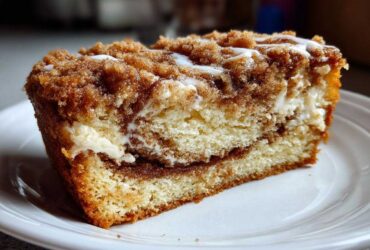 Close-up of a moist slice of coffee cake featuring layers of cake, cream cheese filling, and a thick cinnamon streusel topping.