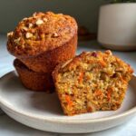 A stack of golden brown morning glory muffins, one cut in half showing carrots and nuts inside.