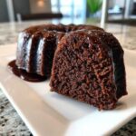 Close-up of a moist, dark chocolate rum cake slice showing the crumb texture, covered in rich chocolate glaze.