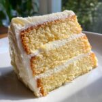Close-up of a moist slice of three-layer vanilla cake recipe, generously frosted with white buttercream.