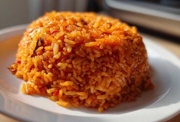 A close-up, featured image of a perfectly molded mound of vibrant orange Nigerian jollof rice on a white plate.