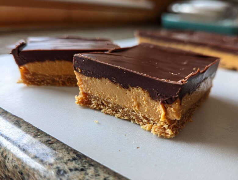 Close-up of two decadent peanut butter bars with a thick chocolate layer on top, showing the crumbly base.