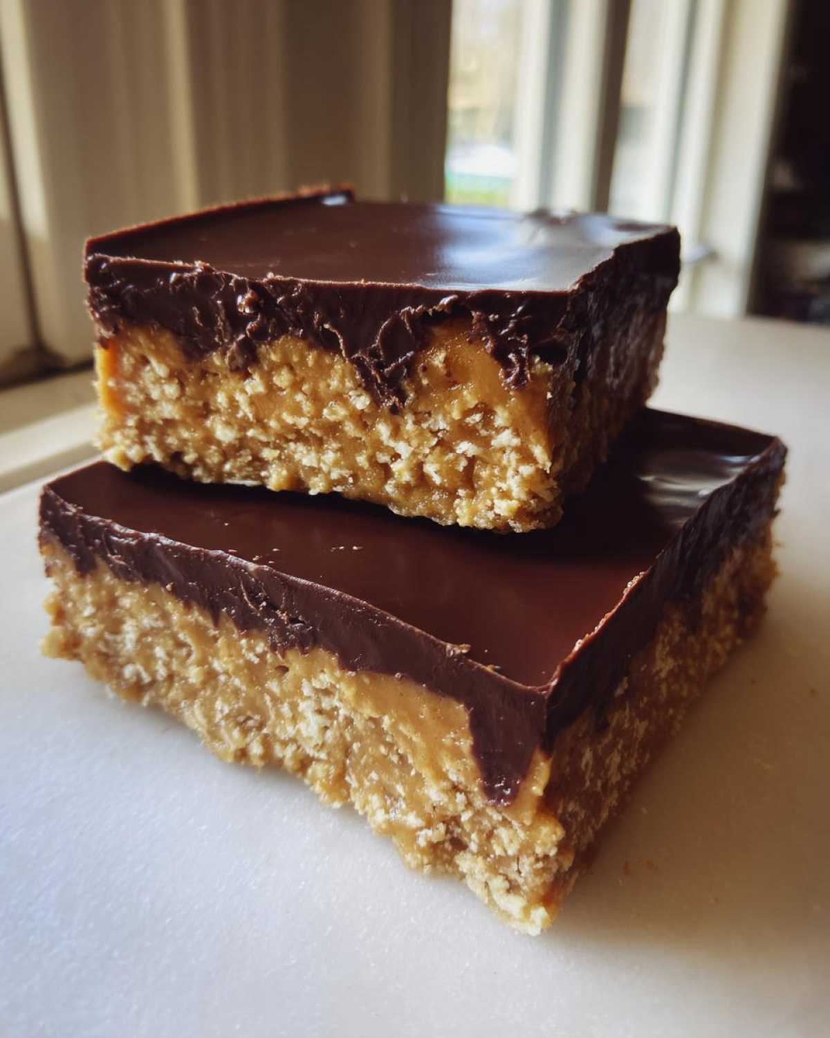 Two rich, layered no bake peanut butter bars stacked, featuring a thick oat base and a smooth chocolate topping.