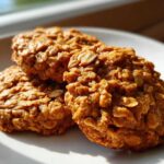 Close-up of three golden brown, textured breakfast cookie treats made with oats, sitting on a white plate.