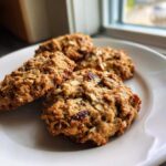 Close-up of four hearty oatmeal breakfast cookie treats piled on a white plate near a window.