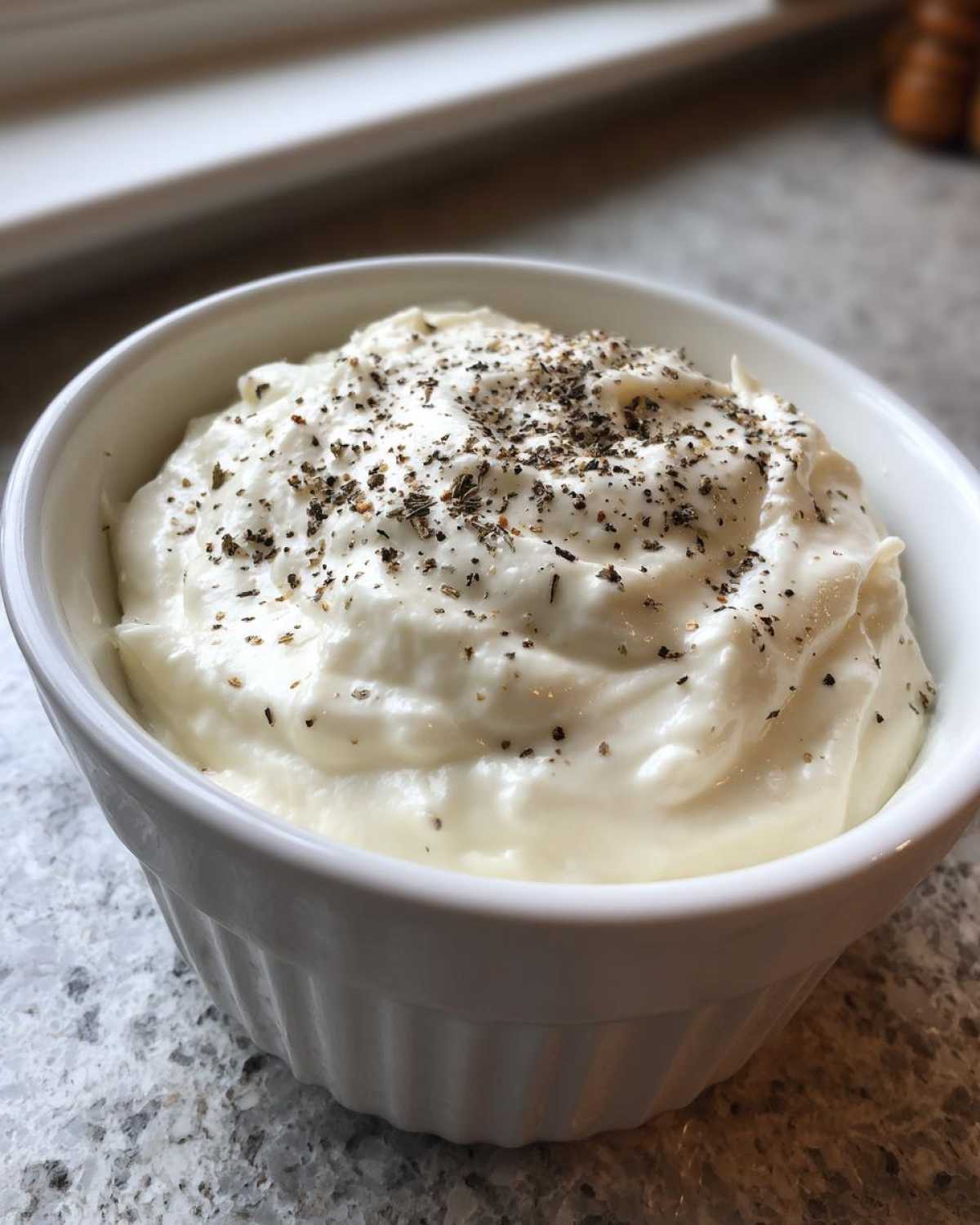 Close-up of creamy Olive Garden Alfredo Sauce topped with black pepper and herbs in a white bowl.