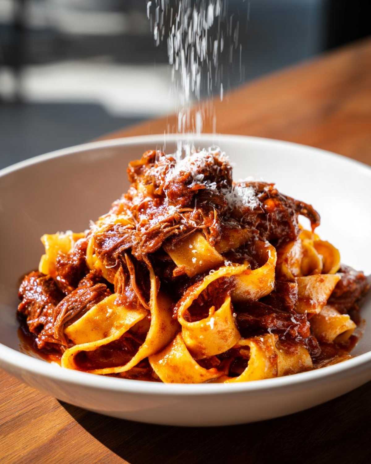 Pappardelle pasta topped with rich beef ragu and grated cheese being sprinkled on top.