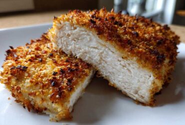 Close-up of parmesan crusted chicken cut in half, showing juicy white meat and crispy golden crust.