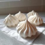 Close-up of five perfectly piped, white meringue cookies resting on a piece of parchment paper.