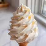 Close-up of perfectly piped, fluffy cream cheese frosting swirl on a sugar cone.