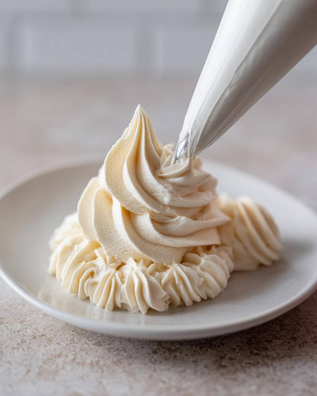 A piping bag dispensing smooth, creamy vanilla buttercream frosting onto a white plate, creating decorative swirls.