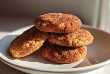 A stack of four soft pumpkin snickerdoodle cookies generously coated in cinnamon sugar, resting on a white plate.